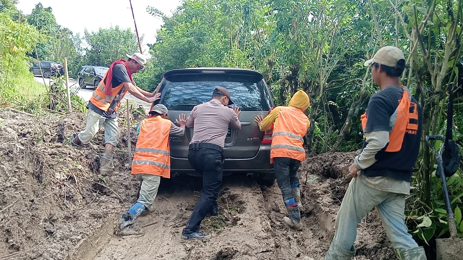 Masyarakat dan Polres Samosir bahu-membahu mendorong sebuah mobil yang terjebak di jalan yang dipenuhi lumpur dan tanah yang disebabkan oleh longsor pada Sabtu pagi, 29 Juni 2024. (ist)